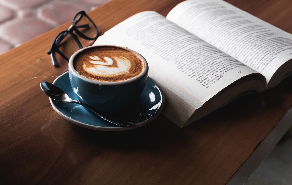 En la imagen se ve una taza de café con libro sobre mesa