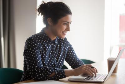 La imagen muestra a una mujer sonriendo frente a una computadora
