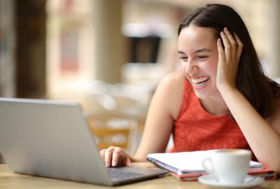 La imagen muestra a una mujer joven sonriendo frente a una computadora