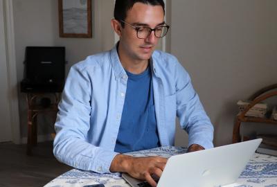 La imagen muestra a un hombre sentado frente a una notebook
