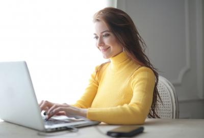 Muchacha sonriendo frente a computadora, tiene un pulóver amarillo