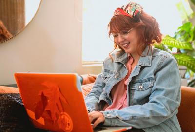 La imagen muestra a una mujer sentada frente a una computadora y sonriendo