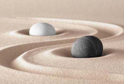 La imagen muestra una fotografía de dos esferas, una blanca y otra negra, sobre arena, representando el ying y el yang