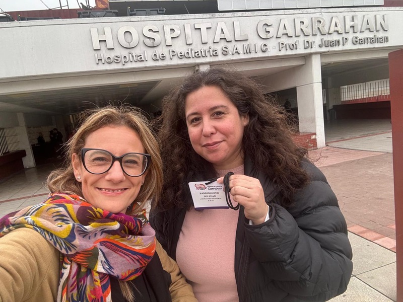 La imagen muestra a la coordinadora académica, Mariana Fullone, junto a una autoridad del Garrahan, frente a la puerta del hispital