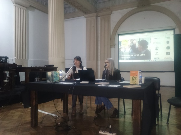 La imagen muestra una foto de las profesoras Cecilia Lasa y Silvia Camerotto dando la charla