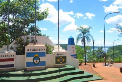 La imagen muestra una fotografía del hito tres fronteras en la Provincia de Misiones. Tiene la forma de un obelisco pintado con los colores de la bandera argentina.