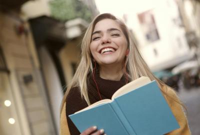 La imagen muestra a una mujer sonriendo sosteniendo un cuaderno en la mano