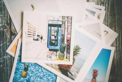 La imagen muestra varias fotos tipo Polaroid sobre una mesa, en una de ellas se ve un teléfono, en otra una piscina y también ananás