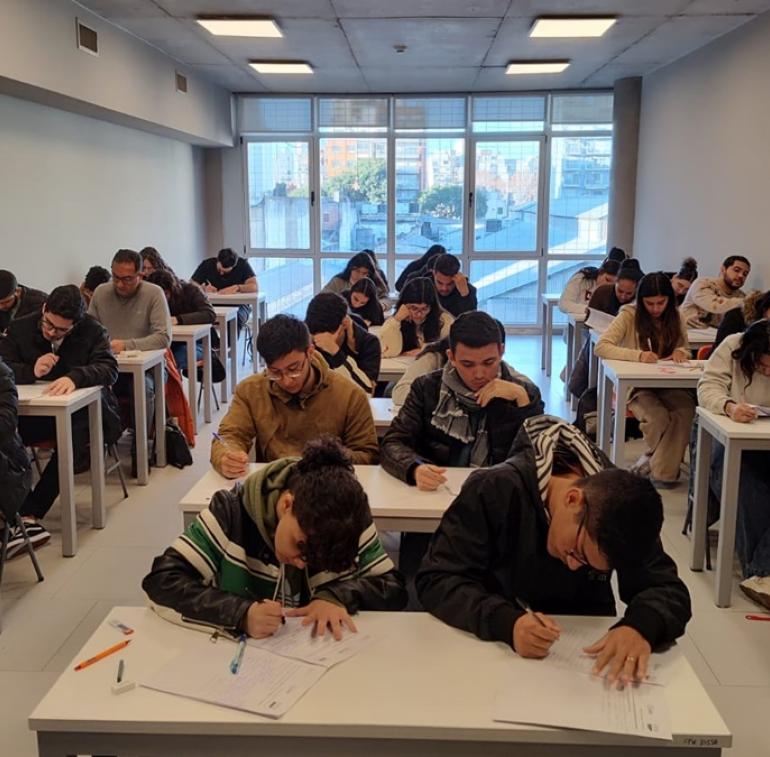 La imagen muetra una foto de estudiantes en un aula rindiendo el CEA en julio de 2024